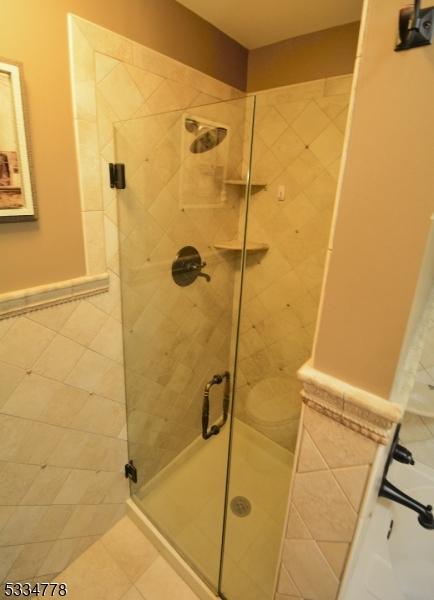 bathroom featuring toilet, a shower with shower door, and tile patterned flooring