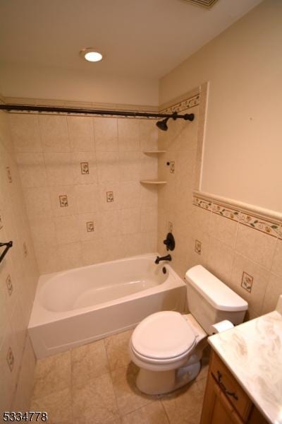 full bathroom with toilet, tile walls, vanity, tiled shower / bath combo, and tile patterned flooring