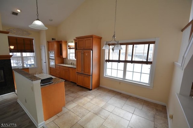 kitchen with light tile patterned floors, decorative light fixtures, high vaulted ceiling, and paneled built in refrigerator