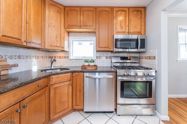 kitchen featuring appliances with stainless steel finishes, sink, decorative backsplash, dark stone counters, and light tile patterned floors