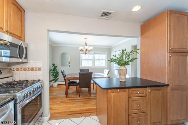 kitchen with appliances with stainless steel finishes, ornamental molding, a notable chandelier, light hardwood / wood-style floors, and backsplash