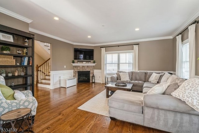 living room featuring dark wood-style floors, ornamental molding, wainscoting, a stone fireplace, and stairs