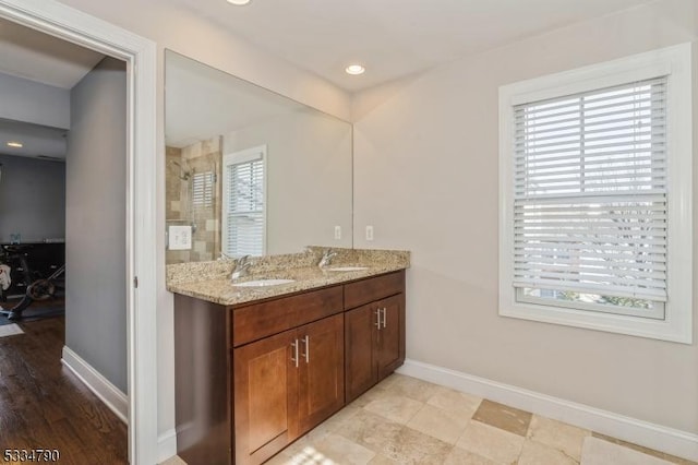 full bathroom with a healthy amount of sunlight, double vanity, baseboards, and a sink