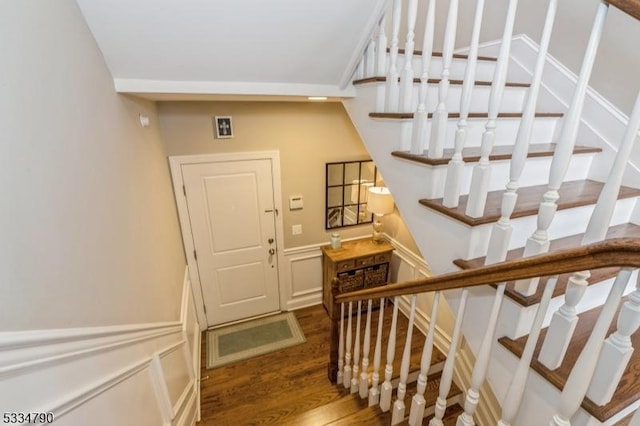 stairs featuring wainscoting, a decorative wall, and wood finished floors