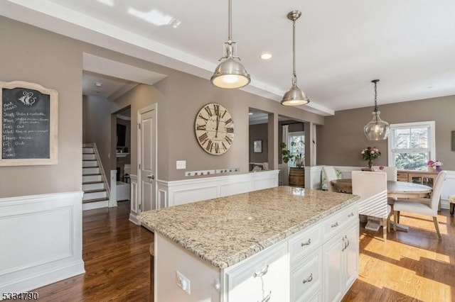 kitchen with wood finished floors, a kitchen island, white cabinetry, wainscoting, and pendant lighting