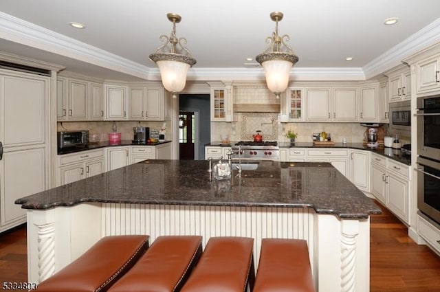 kitchen with hanging light fixtures, dark wood-type flooring, an island with sink, and a breakfast bar