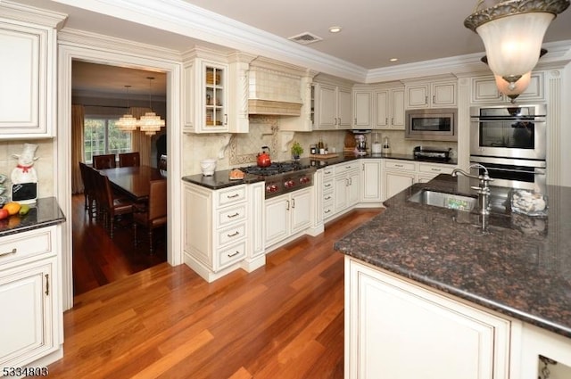 kitchen with sink, custom exhaust hood, appliances with stainless steel finishes, a notable chandelier, and hardwood / wood-style flooring