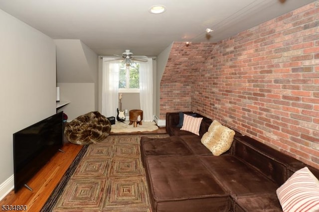 living room featuring hardwood / wood-style flooring, brick wall, a fireplace, and ceiling fan