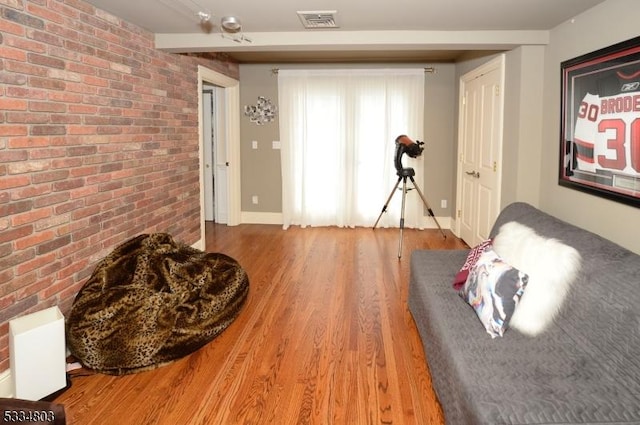 sitting room with brick wall and wood-type flooring