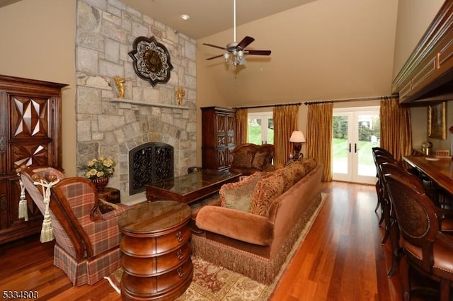 living room featuring french doors, a stone fireplace, hardwood / wood-style floors, and a high ceiling