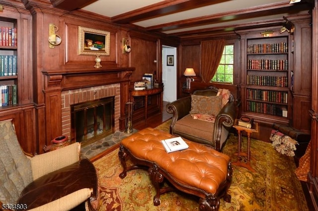 living area with crown molding, a brick fireplace, beam ceiling, and wooden walls