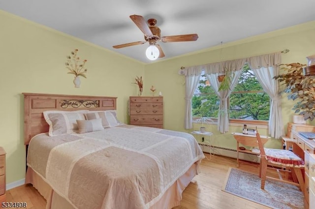bedroom with wood finished floors, a baseboard heating unit, crown molding, a ceiling fan, and baseboards