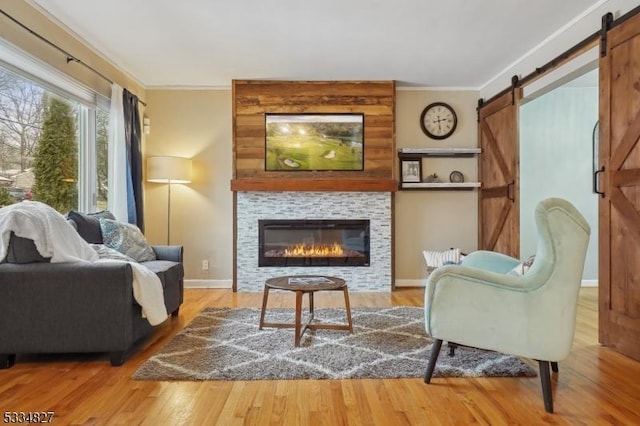 sitting room featuring a tiled fireplace, wood-type flooring, a barn door, and ornamental molding