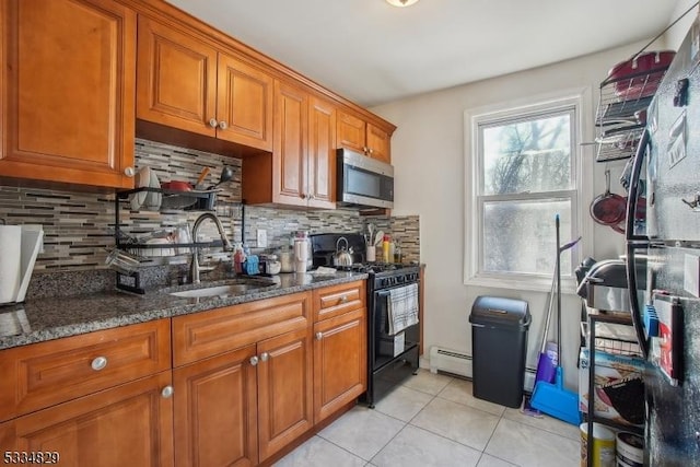 kitchen with sink, light tile patterned floors, black range with gas stovetop, dark stone counters, and a baseboard heating unit