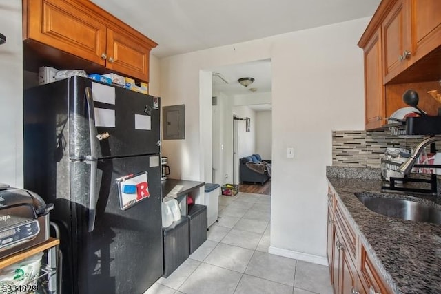 kitchen with tasteful backsplash, sink, dark stone counters, light tile patterned floors, and black fridge