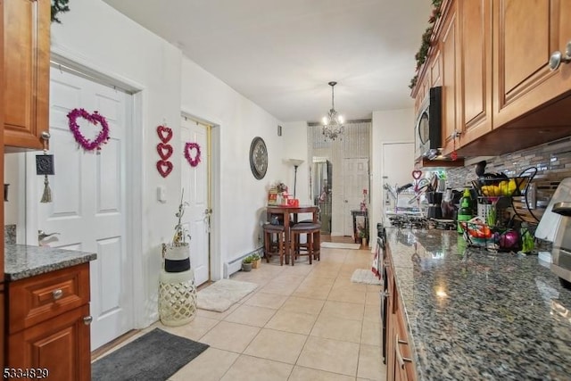 kitchen with tasteful backsplash, a chandelier, dark stone counters, hanging light fixtures, and light tile patterned floors