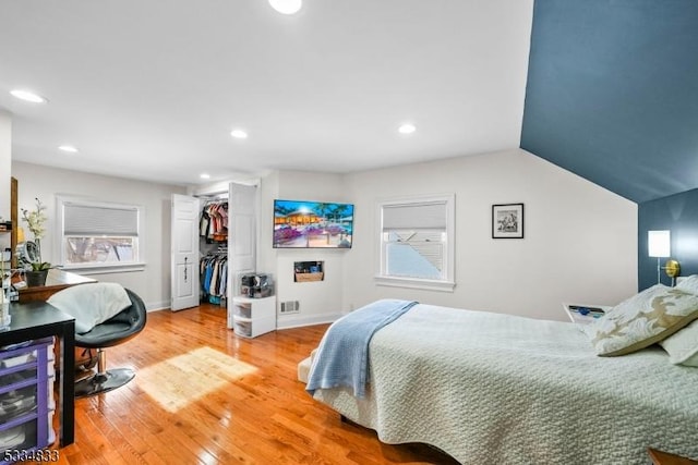 bedroom featuring a walk in closet, lofted ceiling, light hardwood / wood-style floors, and a closet