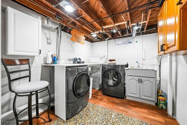 clothes washing area with cabinets, sink, washer and clothes dryer, and light hardwood / wood-style flooring