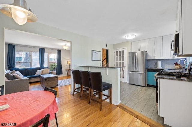 kitchen with a breakfast bar area, stainless steel refrigerator, tasteful backsplash, white cabinets, and light wood-type flooring