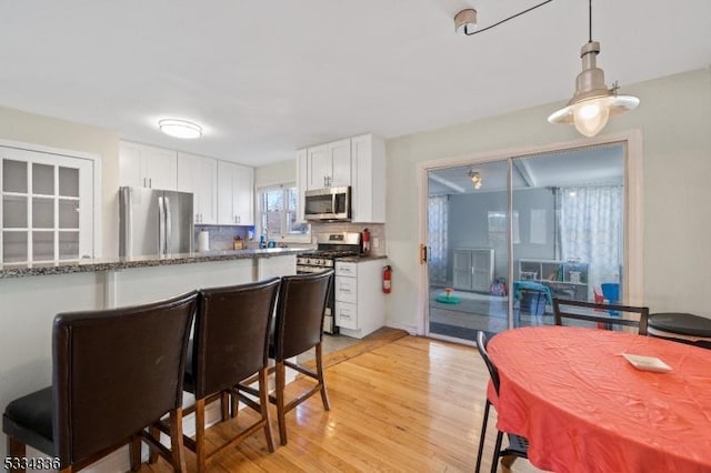 kitchen with white cabinetry, pendant lighting, stainless steel appliances, and light wood-type flooring