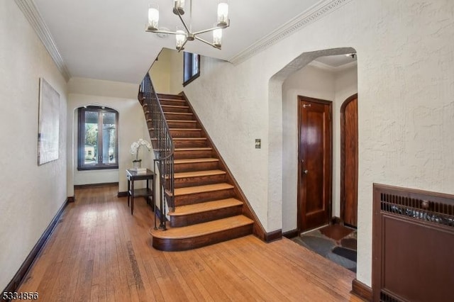 stairs featuring wood-type flooring, ornamental molding, and a chandelier