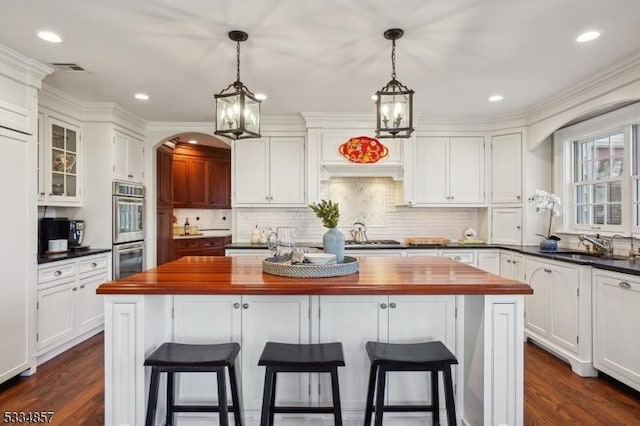 kitchen with double oven, butcher block countertops, white cabinets, and a center island