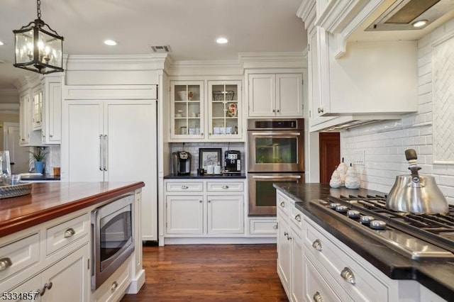 kitchen featuring stainless steel appliances, a sink, hanging light fixtures, dark wood finished floors, and glass insert cabinets