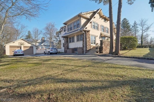 view of front facade with stone siding, a front yard, a detached garage, and stucco siding