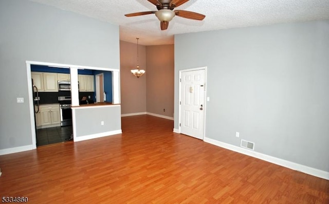 unfurnished living room featuring wood-type flooring, ceiling fan with notable chandelier, a textured ceiling, and a high ceiling