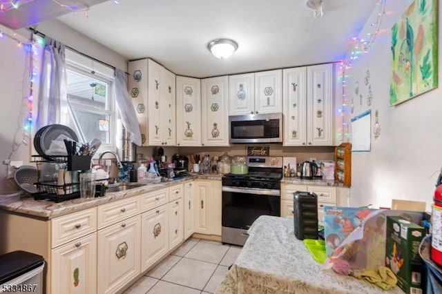 kitchen with light tile patterned flooring, appliances with stainless steel finishes, light stone countertops, and sink