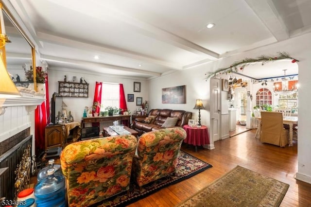 living room featuring hardwood / wood-style flooring, beam ceiling, an inviting chandelier, and a tile fireplace