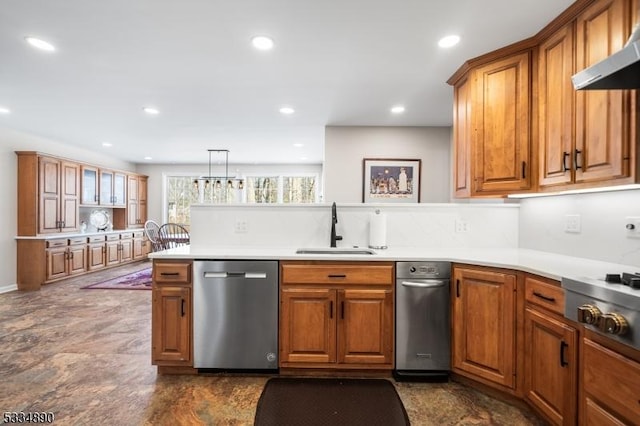 kitchen with a peninsula, a sink, appliances with stainless steel finishes, brown cabinets, and wall chimney exhaust hood