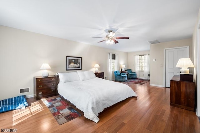 bedroom with a ceiling fan, visible vents, baseboards, and wood finished floors