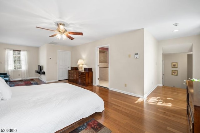 bedroom featuring ceiling fan, ensuite bath, baseboards, and wood finished floors