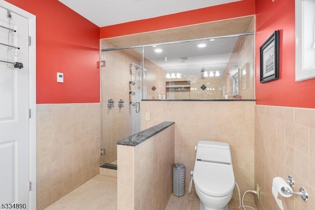 bathroom featuring toilet, wainscoting, a shower stall, and tile walls