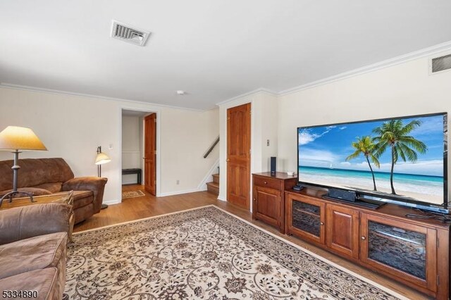 living area with stairway, visible vents, light wood finished floors, and ornamental molding