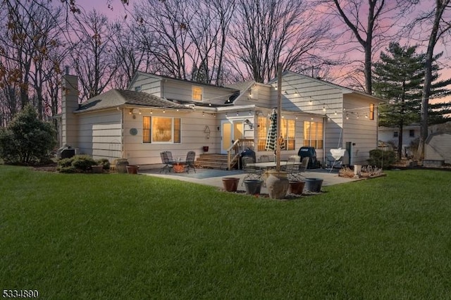 back of property at dusk featuring a patio, a yard, and a chimney