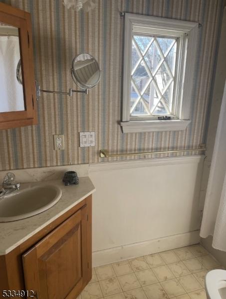 bathroom featuring vanity, toilet, and wallpapered walls