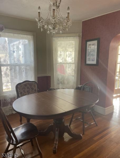 dining space with arched walkways, a chandelier, wood finished floors, baseboards, and crown molding