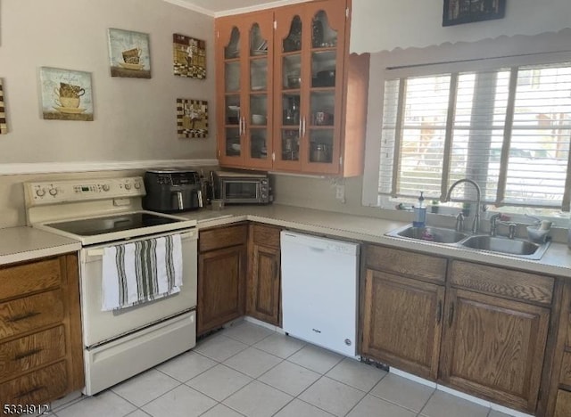 kitchen featuring white appliances, a sink, light countertops, brown cabinets, and glass insert cabinets