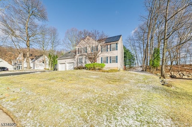 view of front of home featuring a garage, a front lawn, and solar panels