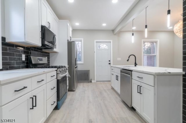 kitchen featuring appliances with stainless steel finishes, radiator heating unit, white cabinetry, sink, and hanging light fixtures