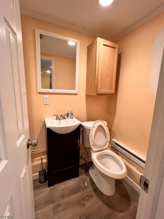 bathroom featuring hardwood / wood-style floors, vanity, ornamental molding, baseboard heating, and toilet