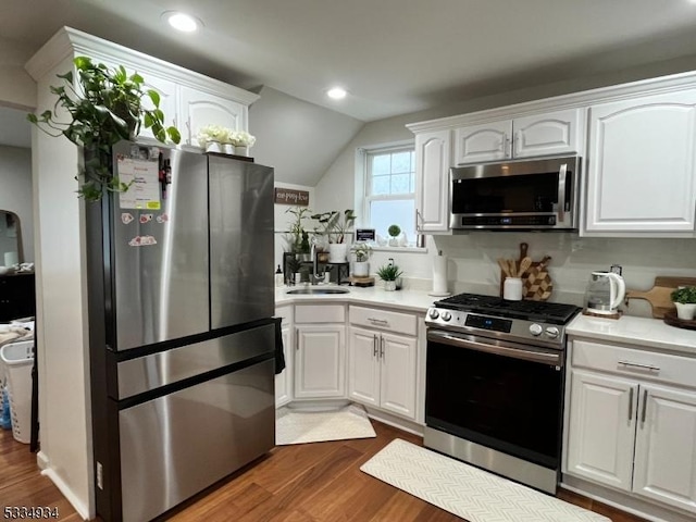 kitchen with appliances with stainless steel finishes, white cabinetry, lofted ceiling, sink, and dark hardwood / wood-style flooring