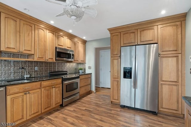 kitchen featuring stainless steel appliances, a sink, backsplash, and light wood finished floors