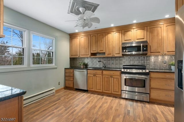 kitchen featuring decorative backsplash, appliances with stainless steel finishes, brown cabinets, baseboard heating, and light wood-style floors