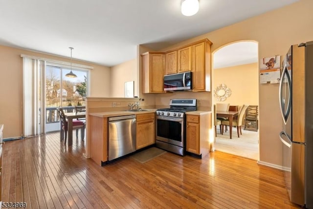 kitchen featuring hardwood / wood-style floors, sink, hanging light fixtures, kitchen peninsula, and stainless steel appliances