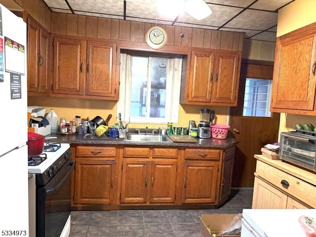 kitchen featuring sink, white appliances, wooden walls, and dark tile patterned flooring