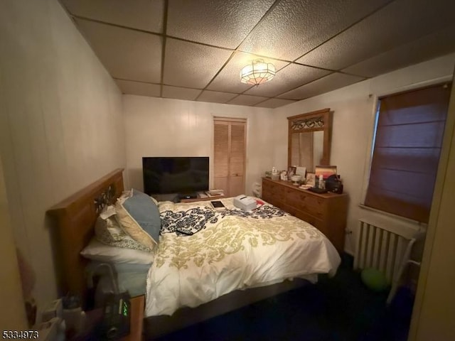 bedroom with a paneled ceiling, radiator heating unit, and a closet