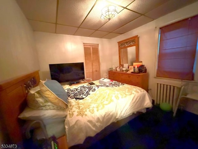 bedroom with a drop ceiling, radiator, and a closet